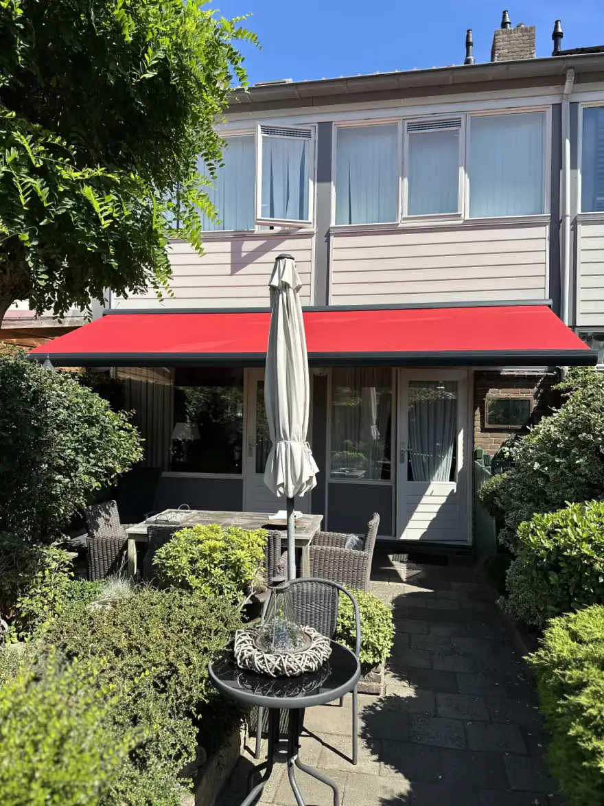 Rood knikarmscherm boven een terras