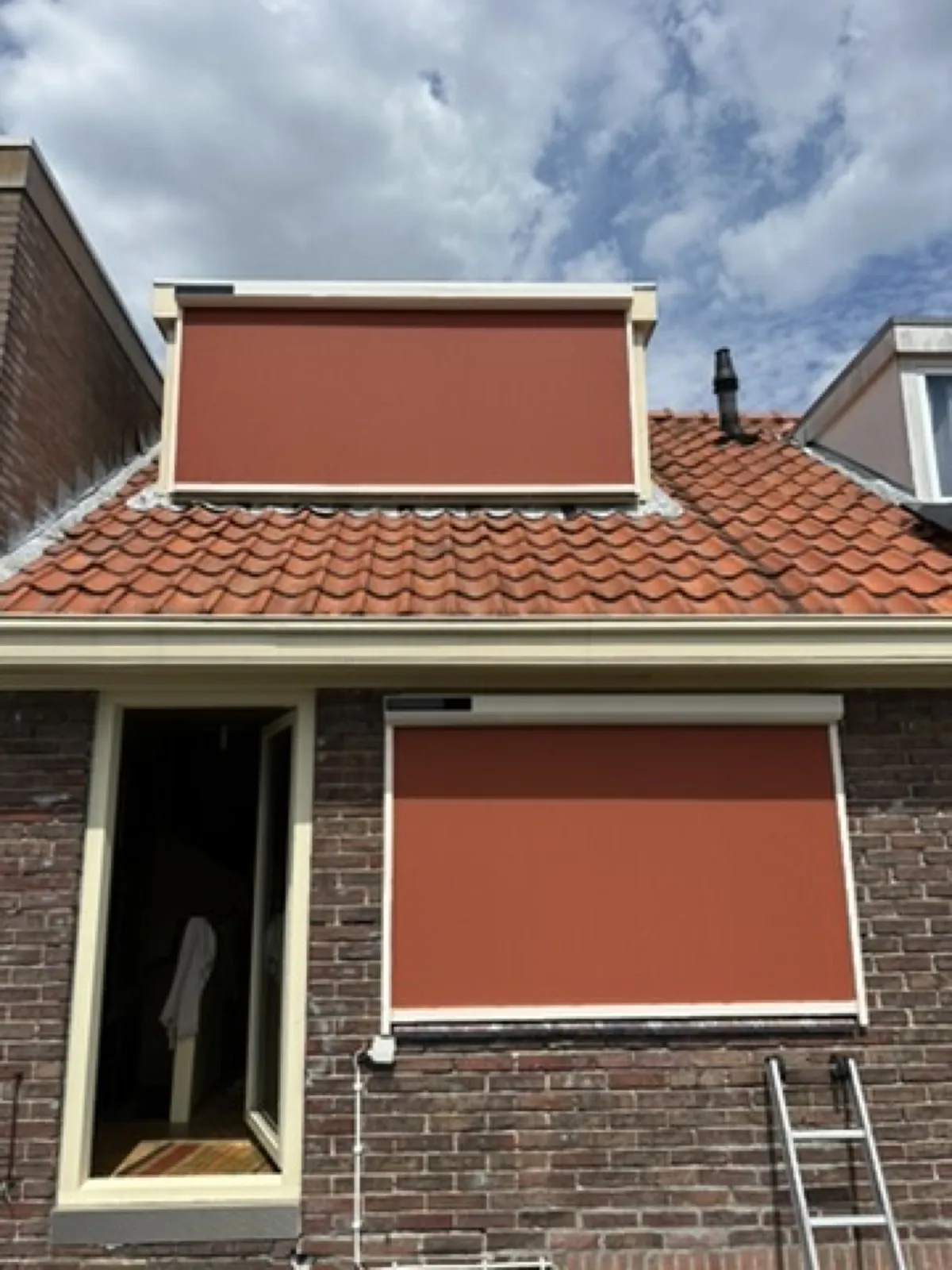 Uitvalscherm met oranje doek boven een raam van een jaren-30-woning
